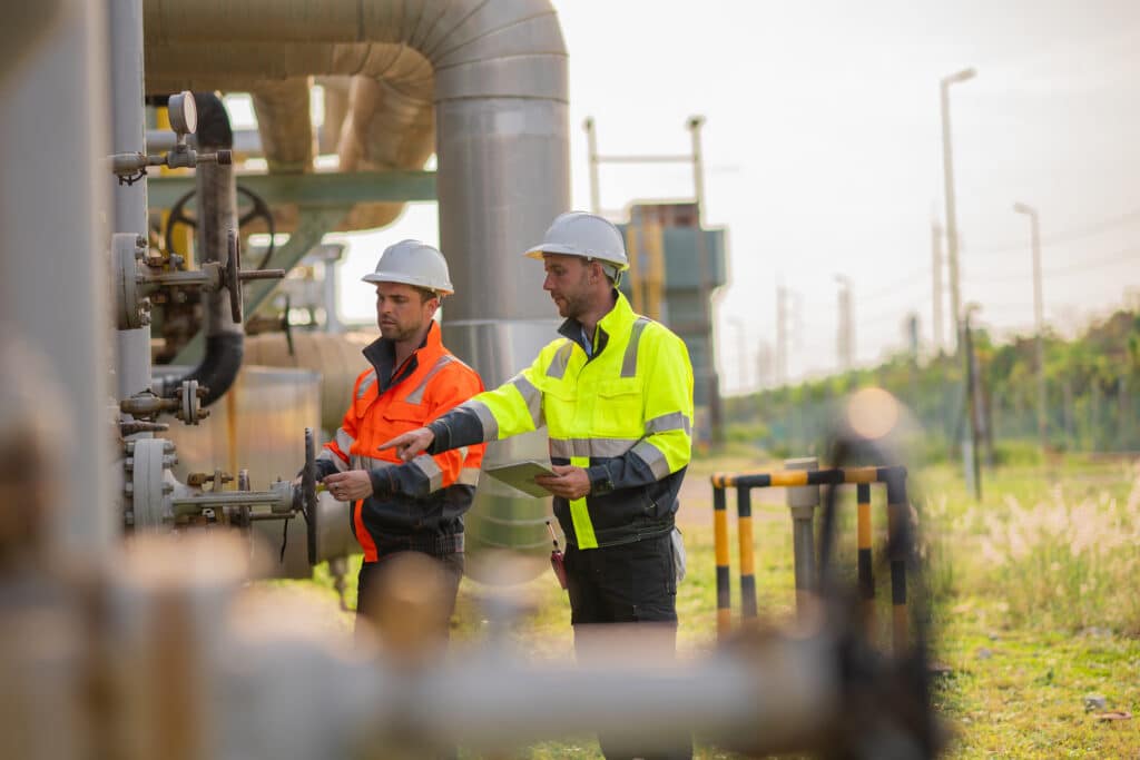 Two industrial workers in safety gear inspecting gas infrastructure and equipment, representing energy operations, maintenance and workplace safety compliance.