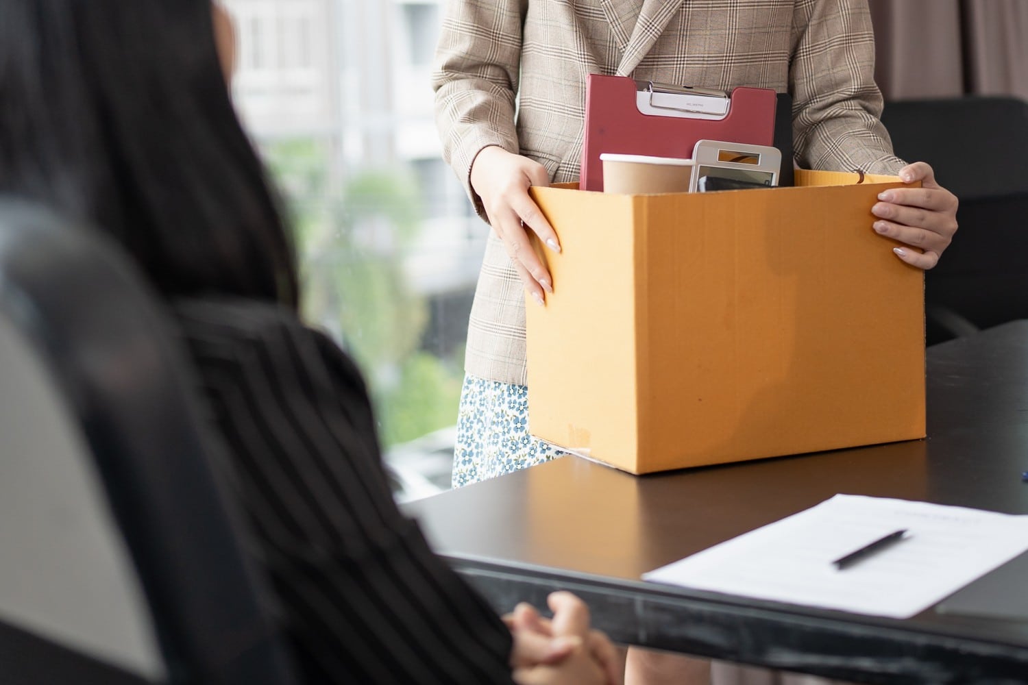 A woman holds a box filled with papers and a folder, symbolising organisation and preparation for redundancy.