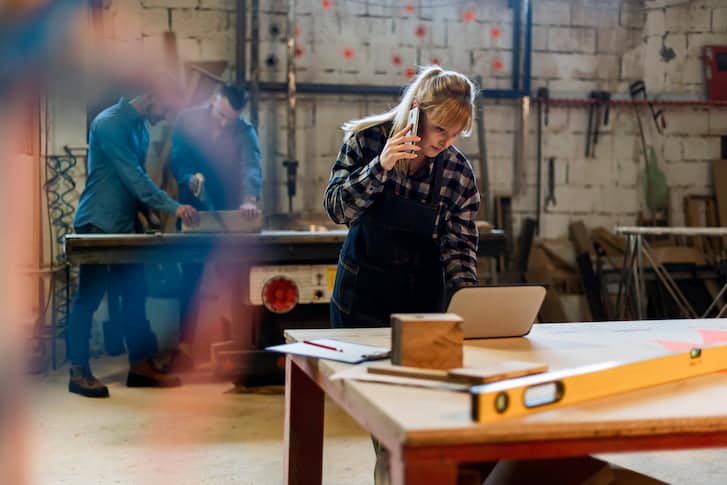 A woman in a workshop engaged in a conversation on her cell phone, surrounded by tools and materials.