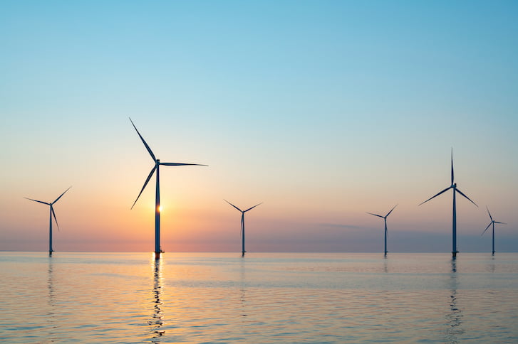 Offshore wind turbines silhouetted against a vibrant sunset over the ocean, showcasing renewable energy in harmony with nature.