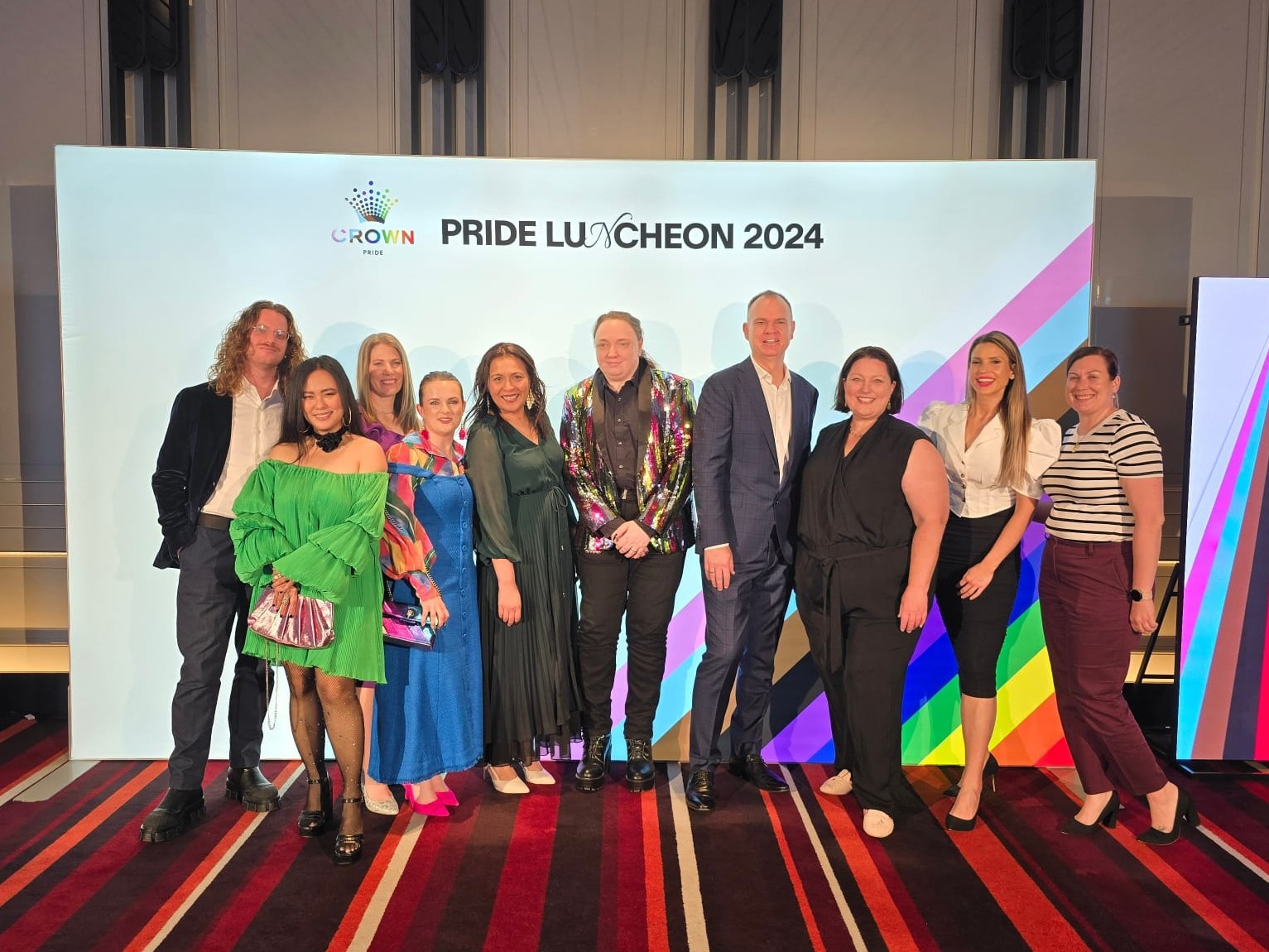 10 people posing in front of a media wall at an event.