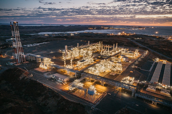 An LNG plant at dusk, illuminated by the warm glow of the setting sun against a colorful sky.