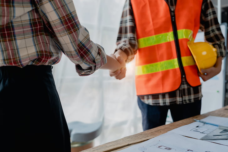 Two professionals shaking hands at a construction site, representing a successful contract negotiation for a tender.