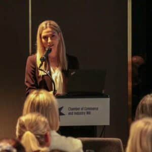 Woman delivering a presentation to a room of people, standing at a lectern.