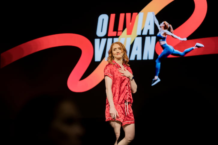 A woman on stage presenting, wearing red pyjamas.