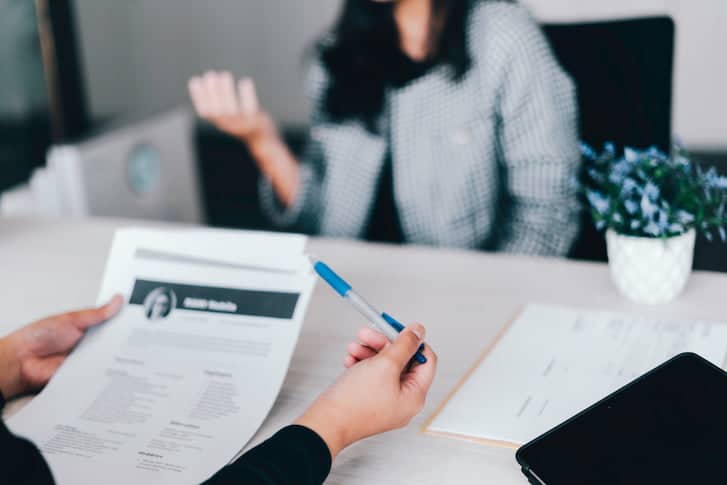 A woman sitting at a desk holds a piece of paper, preparing for a job interview.