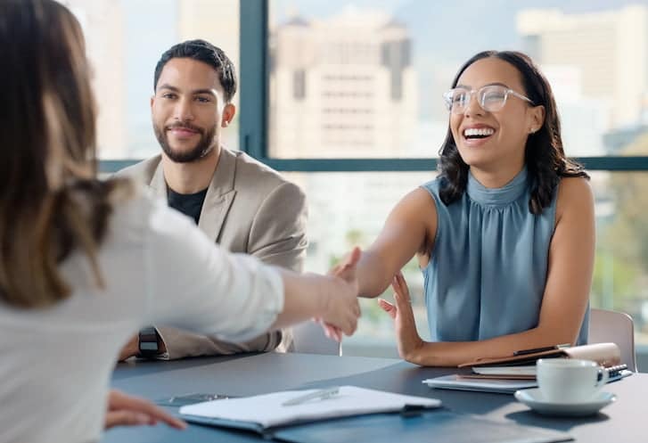 A woman shakes hands with a woman and a man during a job interview meeting, symbolising professional engagement and recruitment.