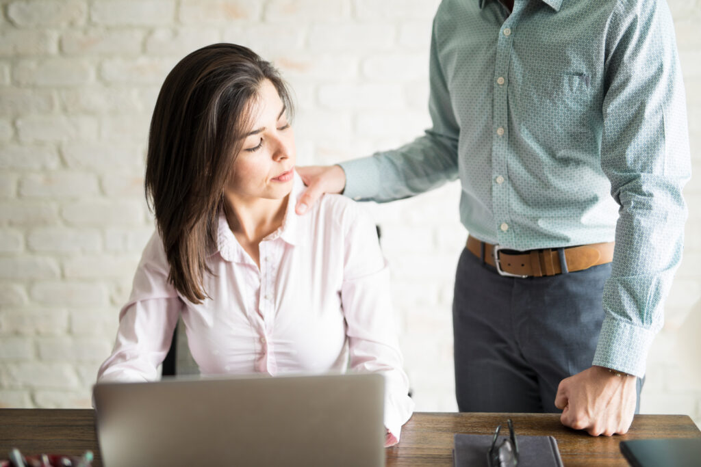 Abusive boss harassing a female colleague in the office while she looks uncomfortable and upset.