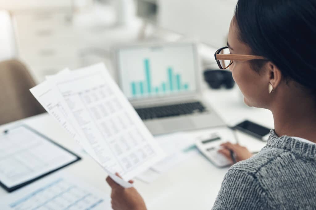 Business_Woman_Payroll_Wages A woman reviews a payroll document on a desk, focusing on wage details.