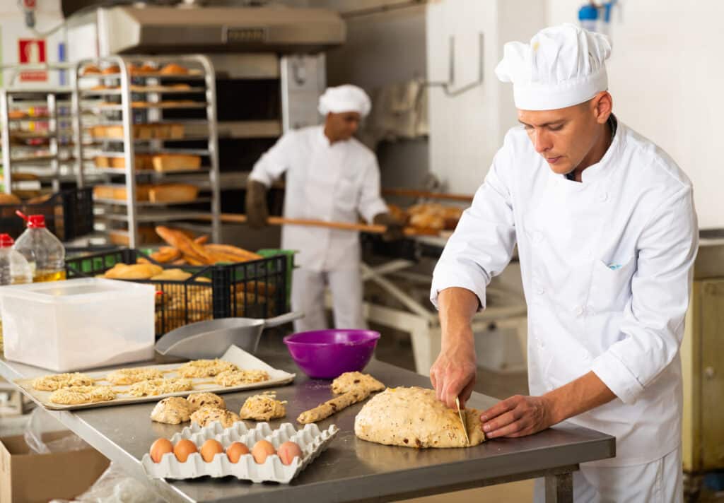 A man in a white uniform working in a food manufacturing facility.