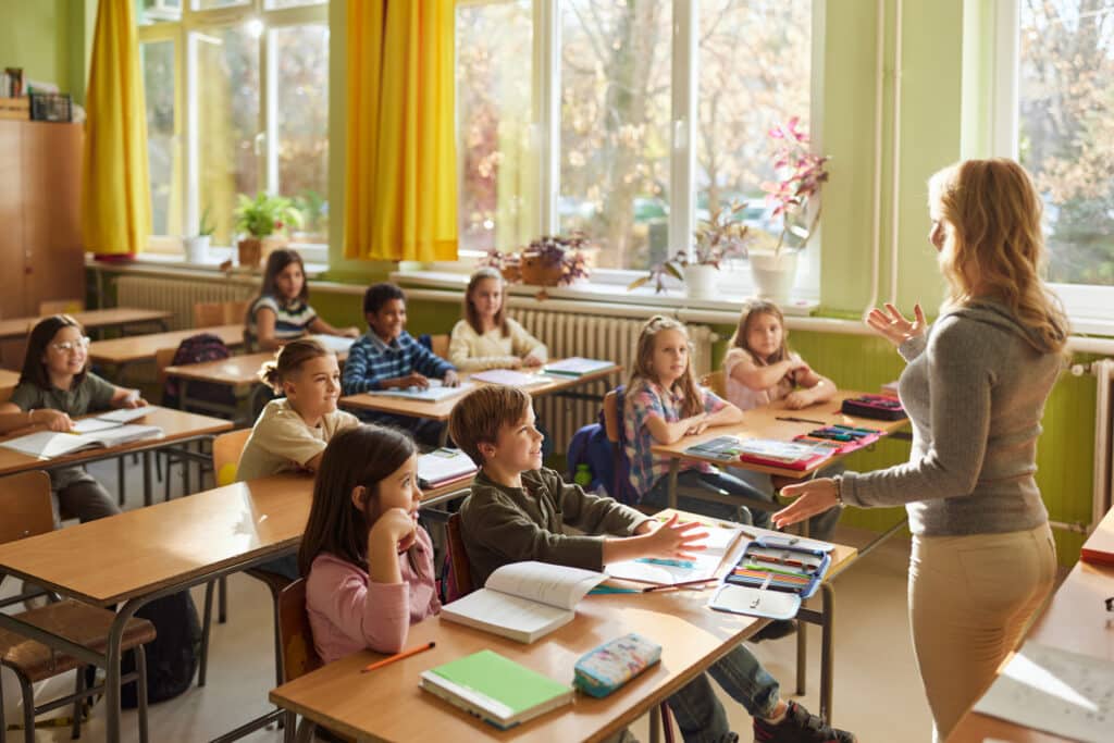 Large group of primary school students listening to their female teacher during a class at school.