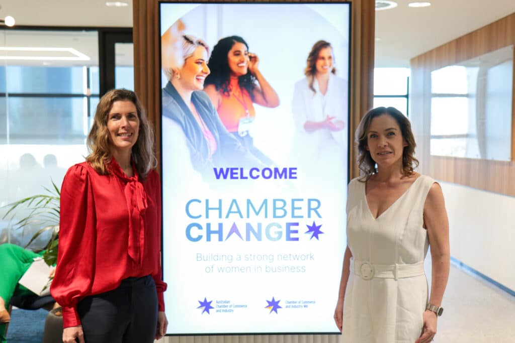 Two women standing beside a Chamber Change welcome sign at a business networking event, promoting a program to build a strong network of women in business.