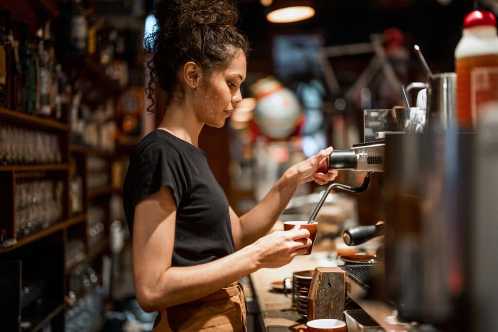 Barista preparing a coffee at an espresso machine in a busy café, showcasing hospitality and small business service.