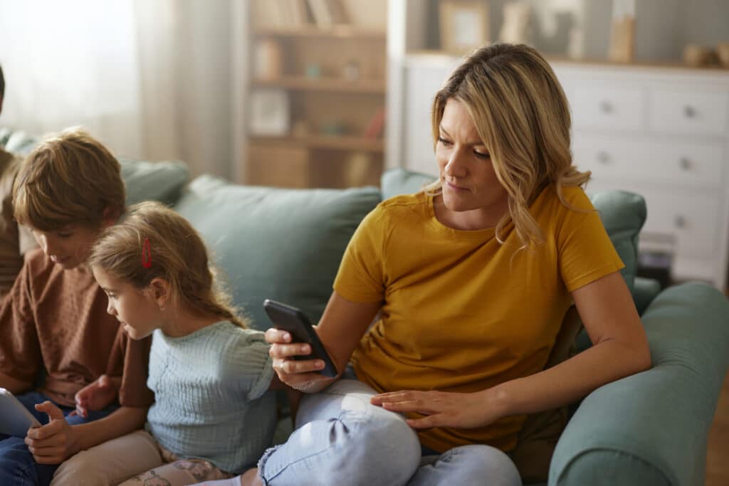 A woman focused on her mobile phone while two children play next to her, suggesting the right to disconnect from work.