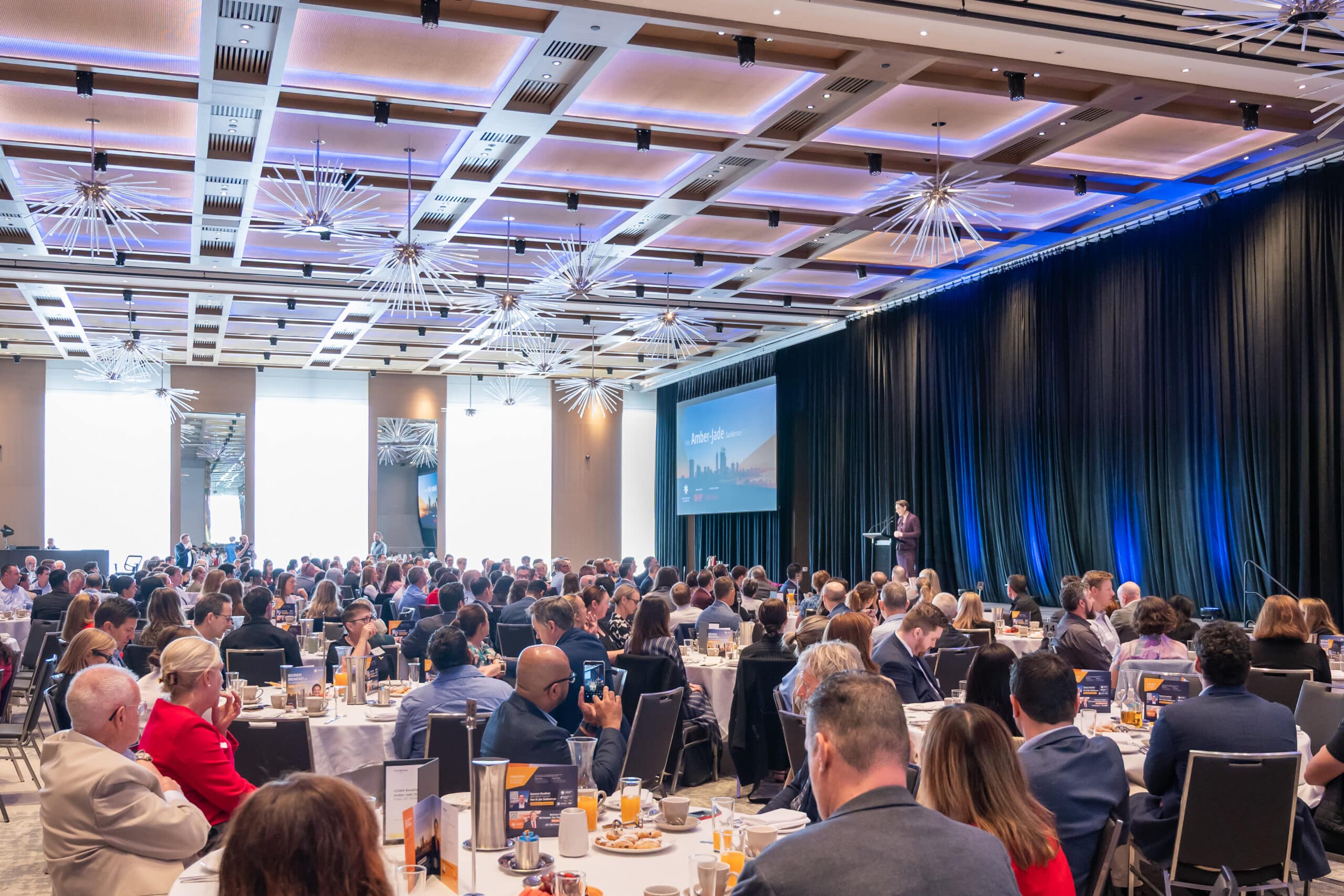 A large group of people seated at tables in a spacious room, engaged in conversation and activities.