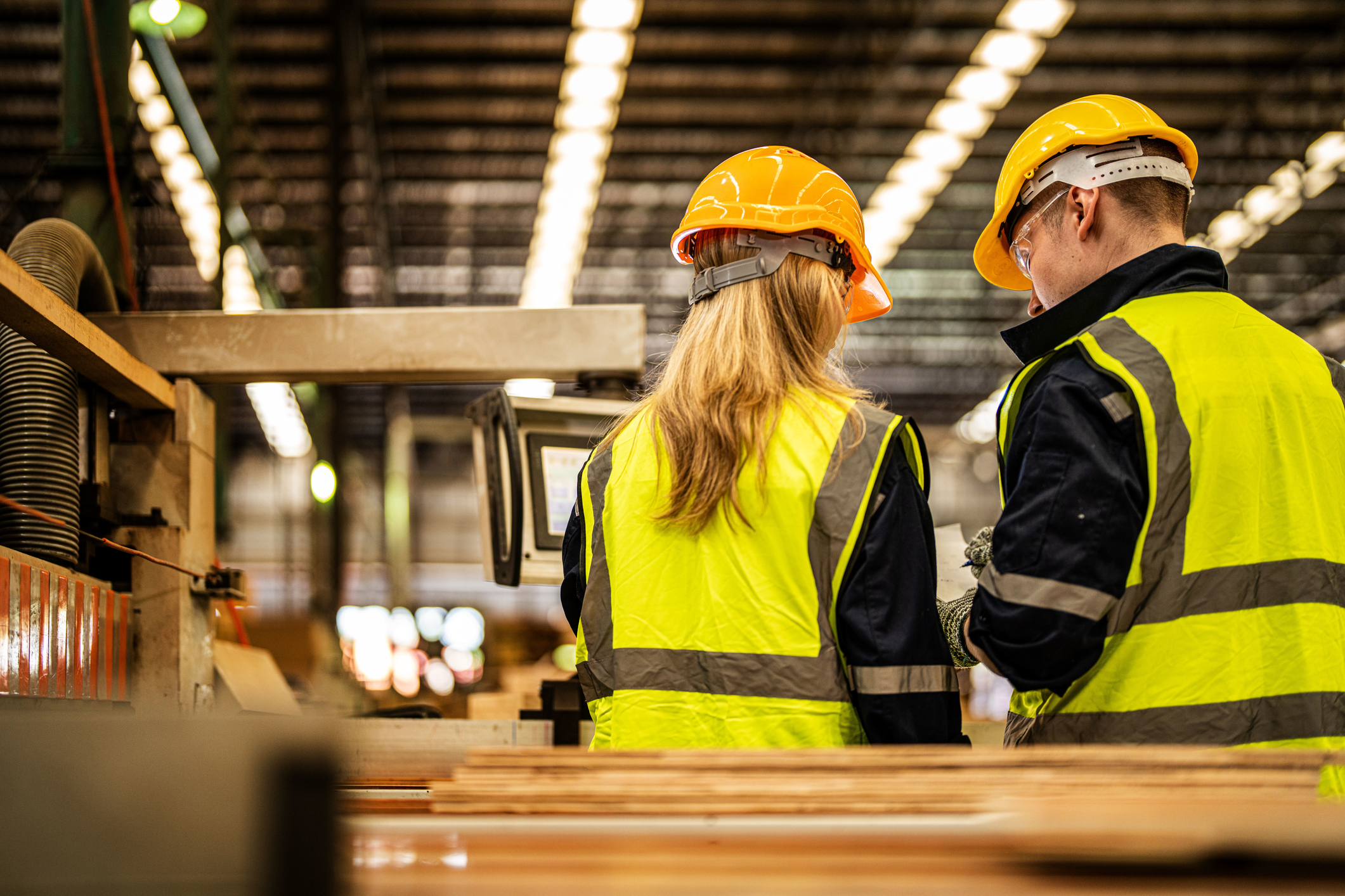 Two workers in safety vests collaborate in a factory, emphasizing work health and safety practices.