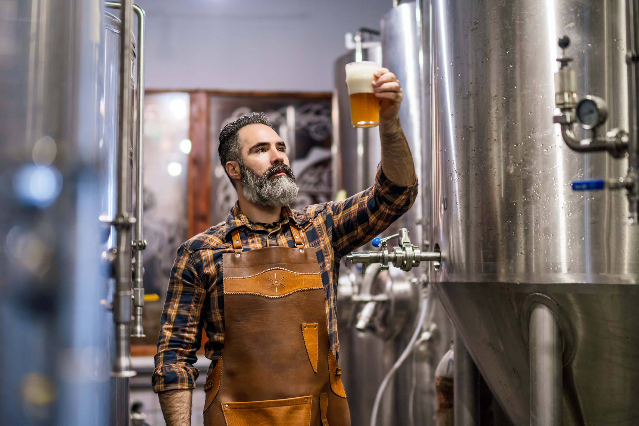 A man holds a beer glass outside a brewery, representing the beverage manufacturing industry.