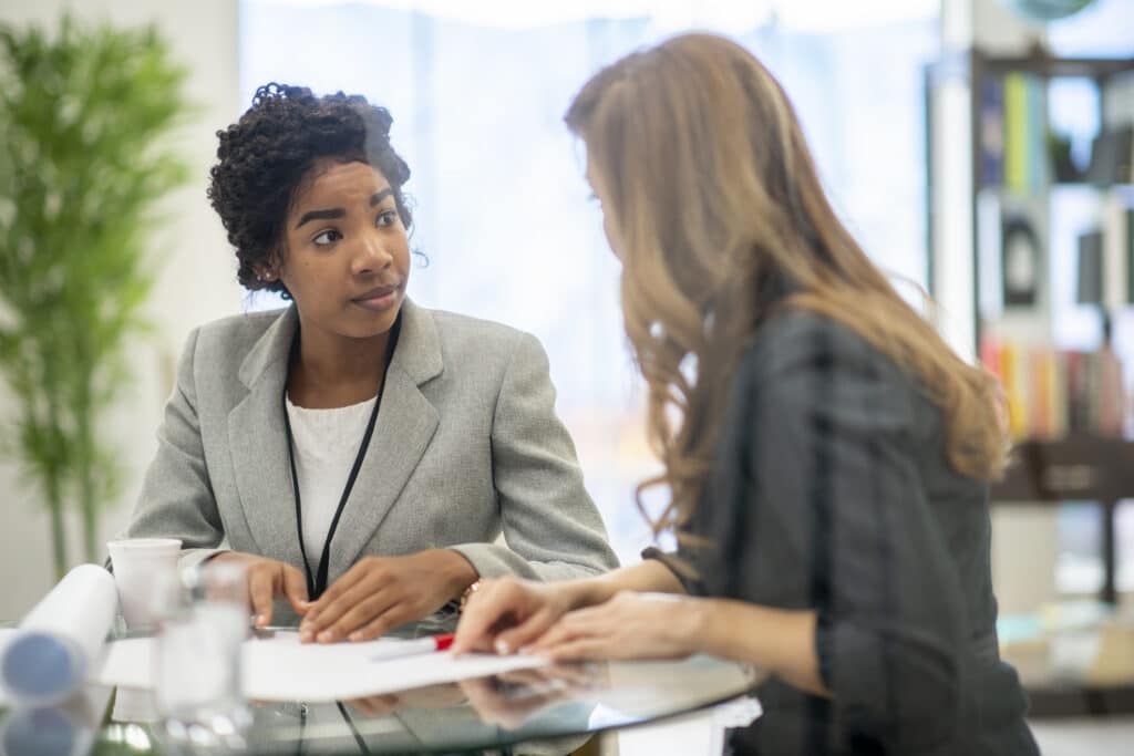 Two professionals seated at a desk in an office discussing documents during a meeting, representing workplace mediation and investigation in a professional, supportive business environment.