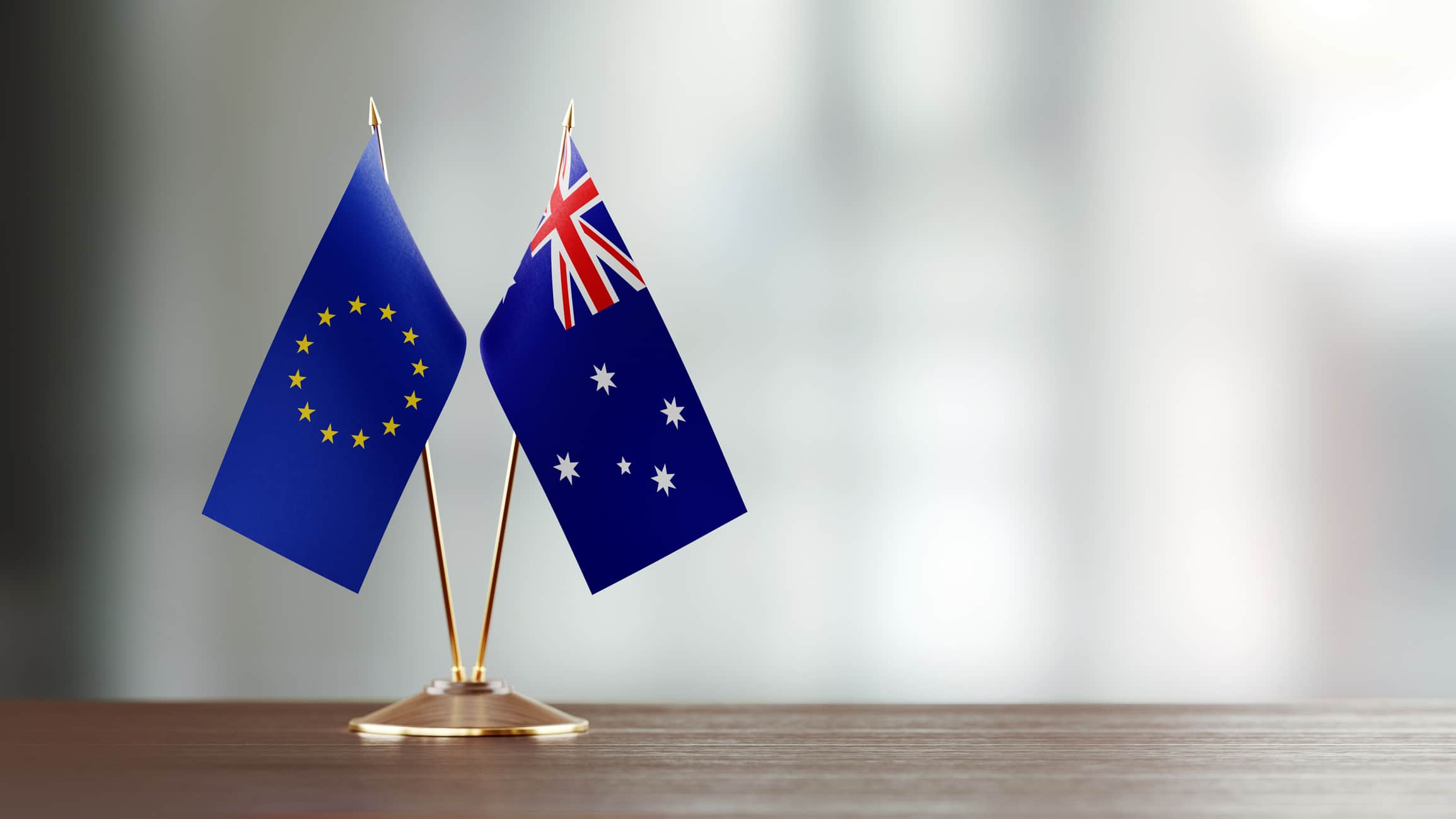 European Union and Australian flag pair on desk over defocused background.
