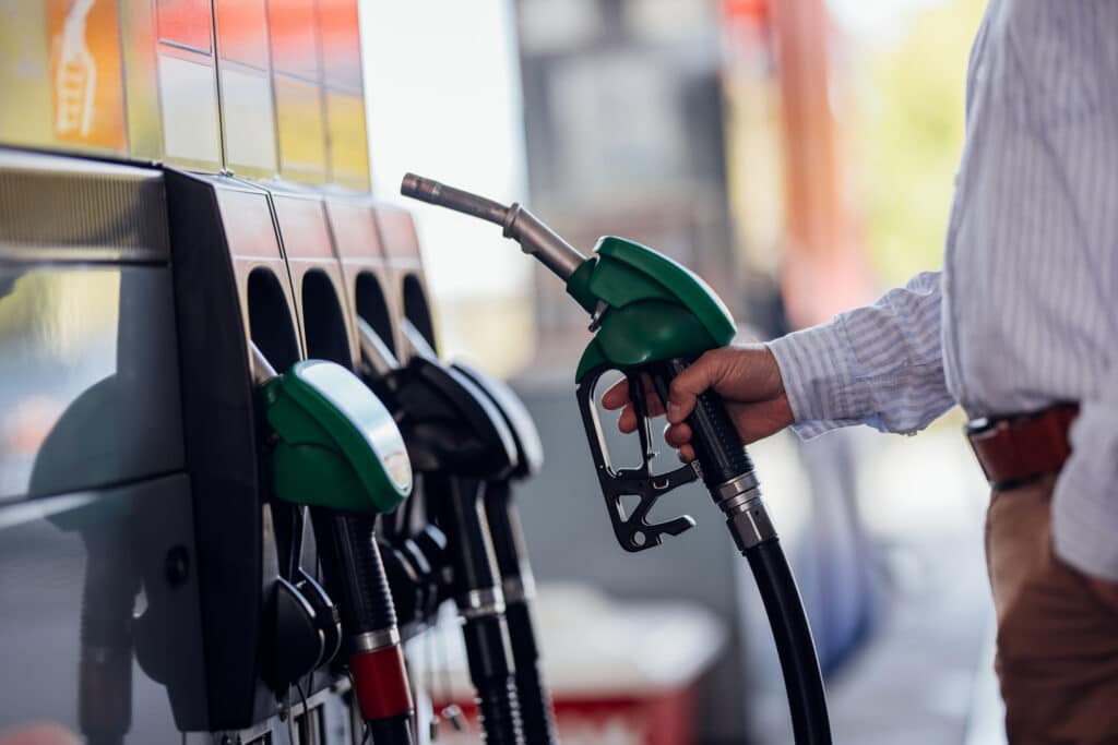 Person holding a fuel pump nozzle at a petrol station, representing fuel supply, pricing pressures and impacts on business operating costs.