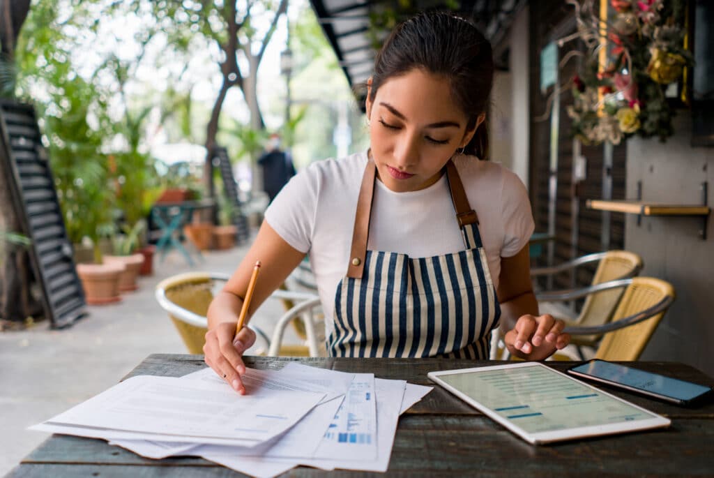 A small business owner writes on paper while seated at a table, focusing on payroll and employee superannuation.