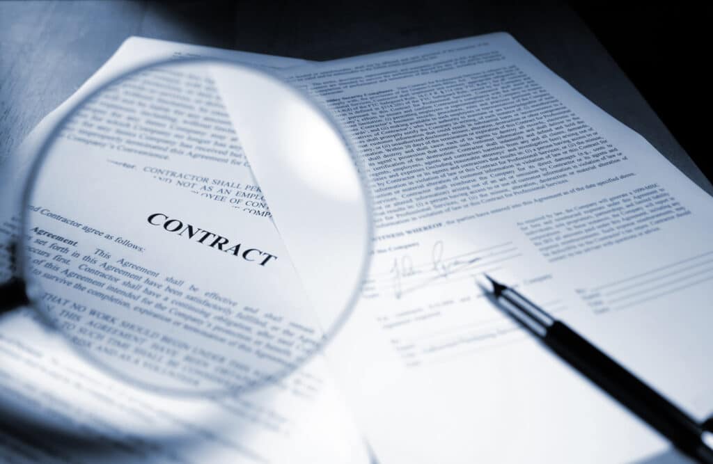 Close-up of a business contract document with a magnifying glass and pen, representing legal review, contractual obligations and risk management in business.