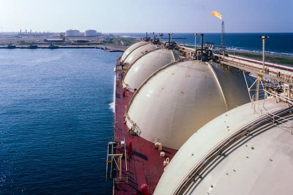 LNG tanker docked at a coastal terminal with storage tanks and infrastructure, representing gas export operations, energy supply chains and maritime logistics.