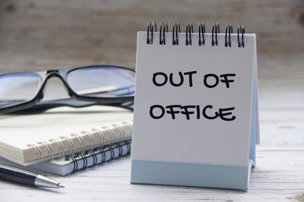 Desk calendar displaying “Out of Office” beside glasses and a notebook, representing annual leave, public holidays and employee absence in the workplace.