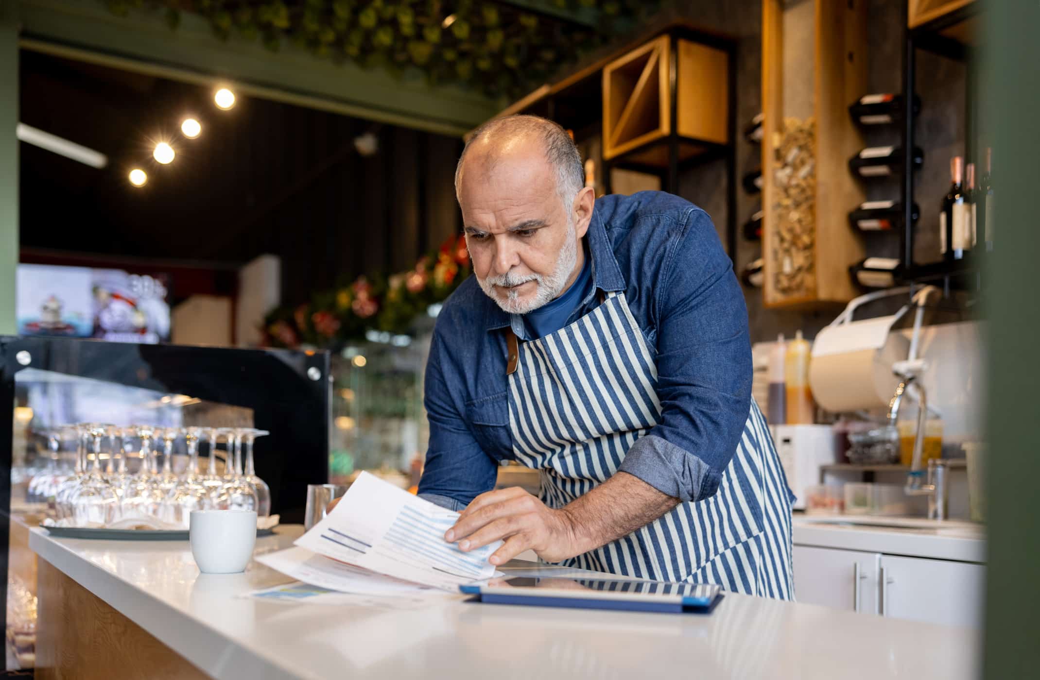 Small business owner bookkeeping at a cafe while looking at some bills.