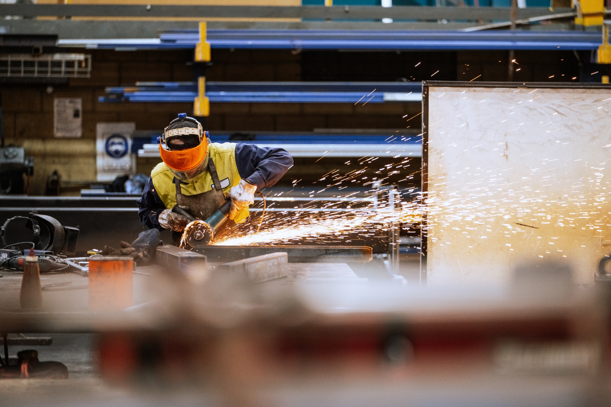 Manufacturing worker using an angle grinder on metal components inside an industrial workshop, with sparks flying during fabrication work.