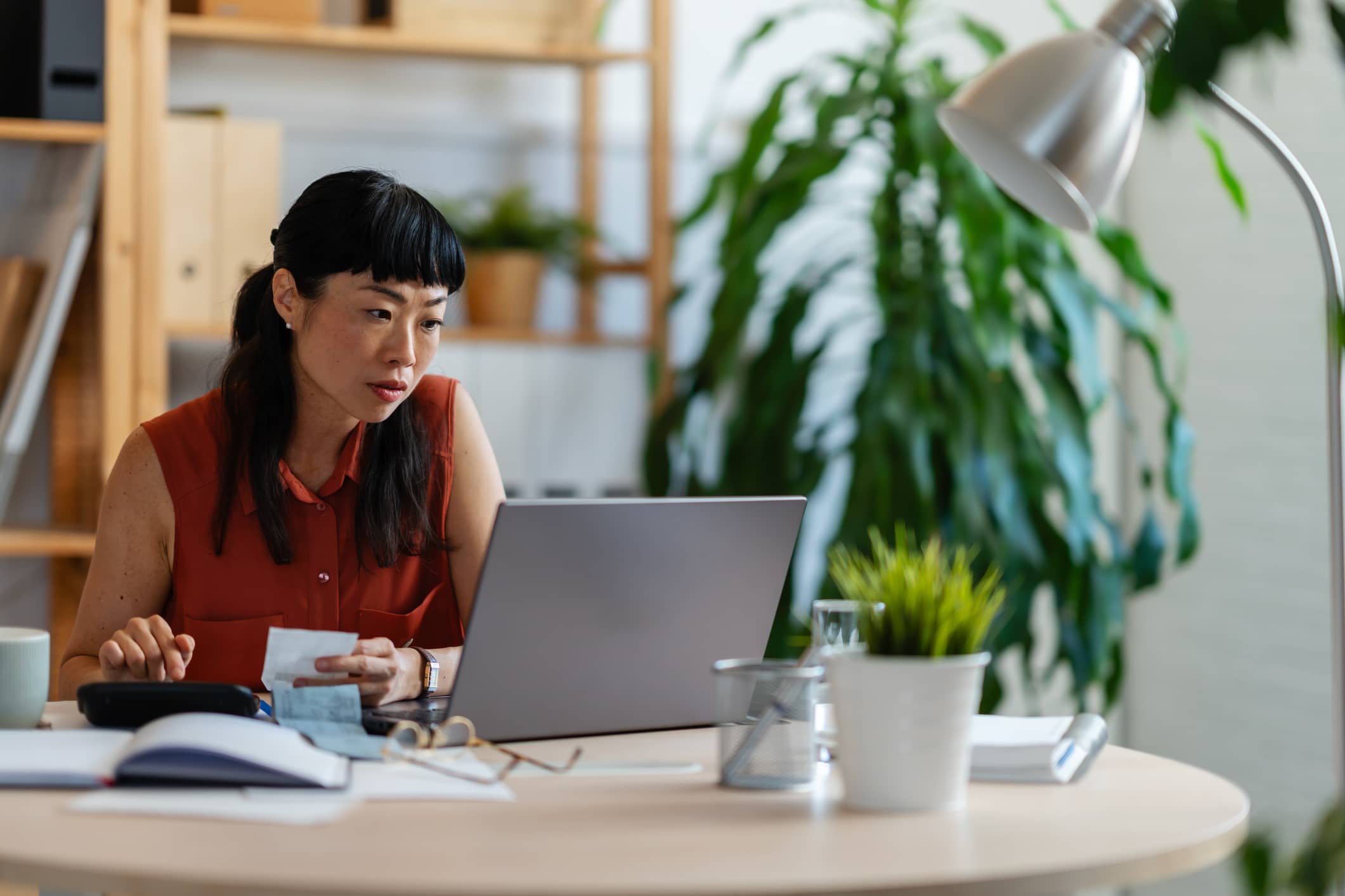 Small business owner reviewing receipts and financial documents while working on a laptop, highlighting tax preparation, accounting and accounts management, bookkeeping and small business finances.