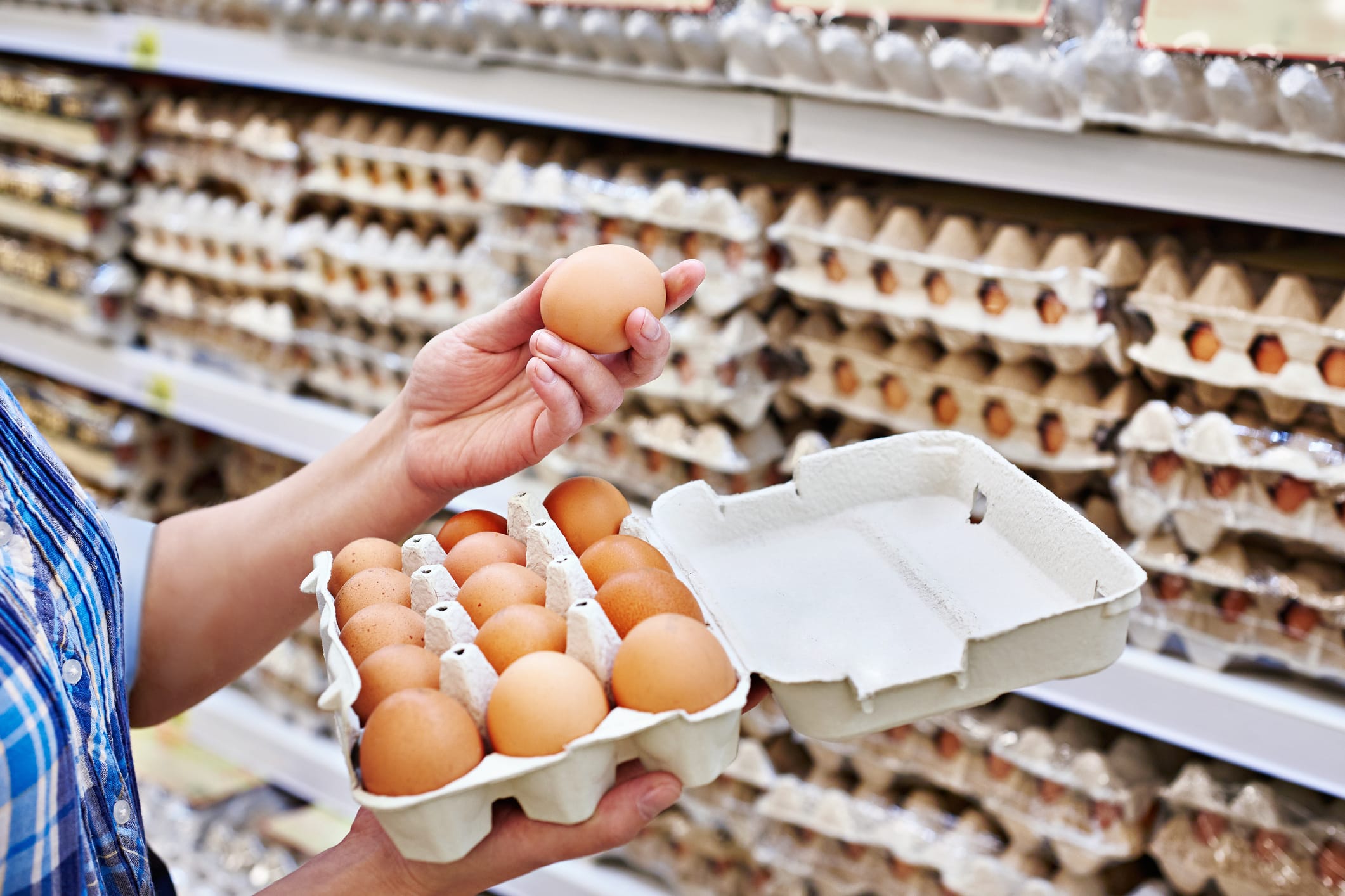 Shopper selecting eggs from a carton in a supermarket aisle, highlighting egg supply, retail, agriculture and the poultry industry.