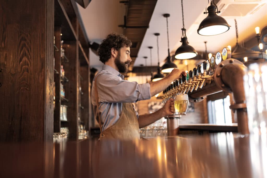 Bartender pouring beer from tap in a busy pub, representing liquor licensing compliance for licensed hospitality venues.