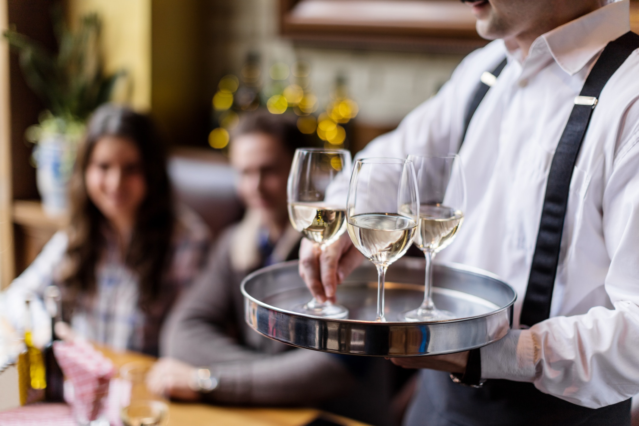 Waiter serving glasses of white wine to diners in a restaurant, highlighting liquor licensing requirements for hospitality businesses.
