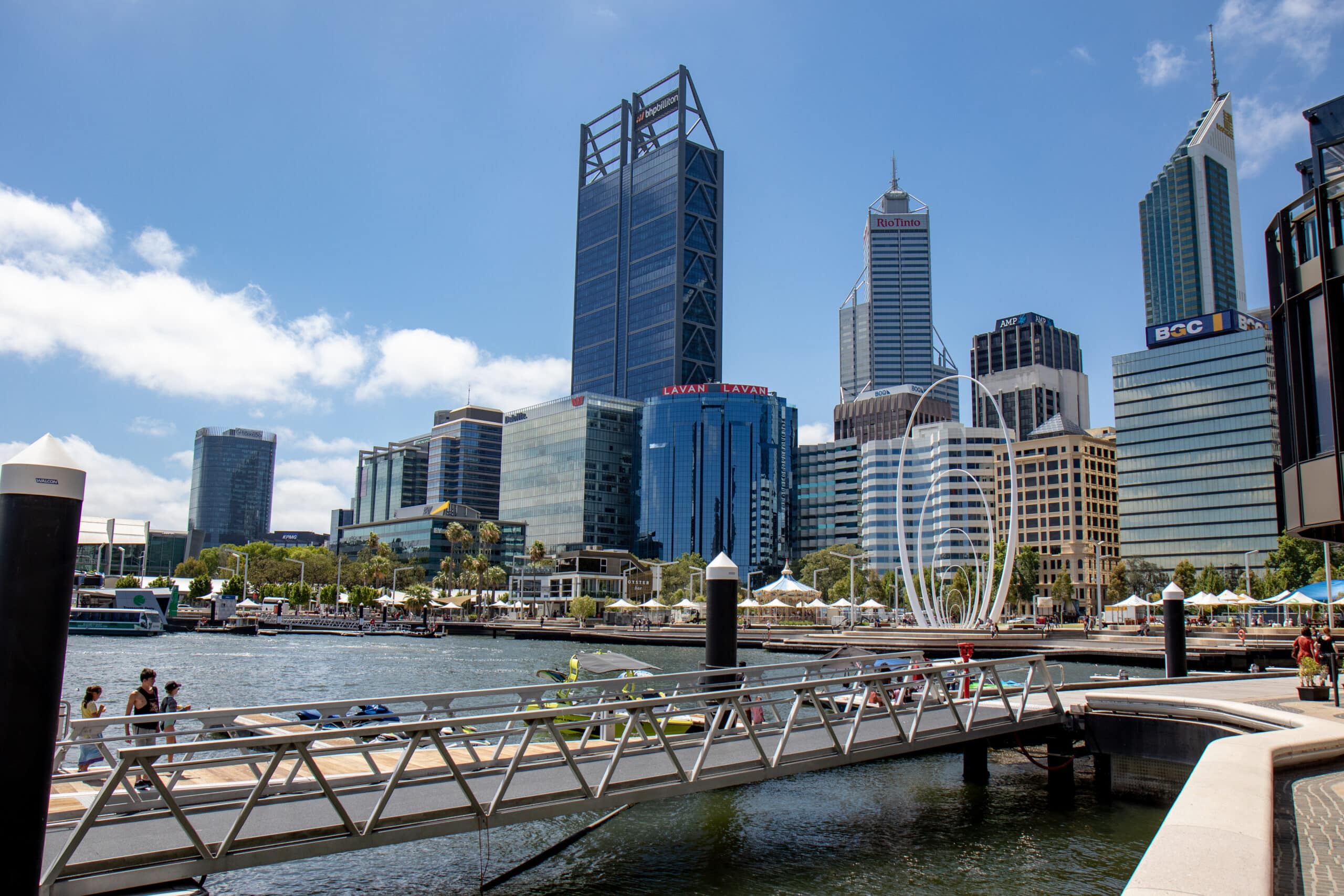 Perth, Western Australia, city skyline viewed across Elizabeth Quay, with office towers, waterfront buildings and the Elizabeth Quay sculpture under a blue sky.