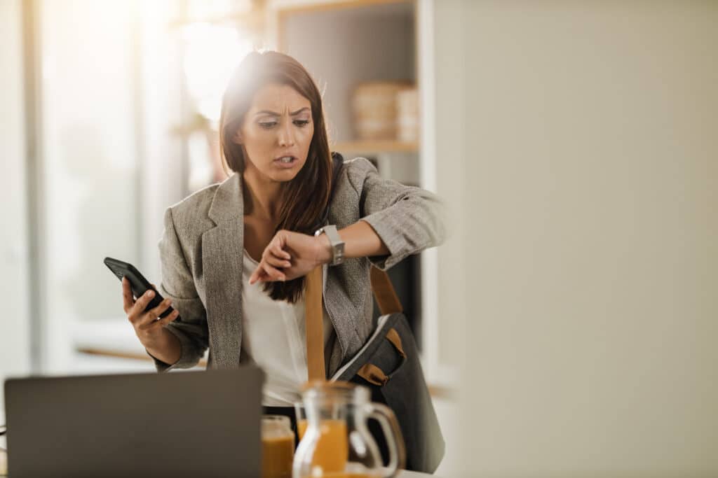 Employee checking her watch while holding a mobile phone, illustrating the right to disconnect from work outside working hours.