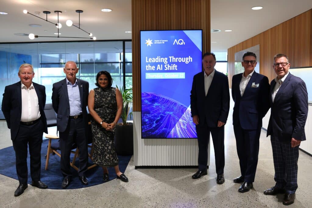 Six people standing beside a screen promoting the CCIWA and AQi event Leading Through the AI Shift on Thursday, October 22.