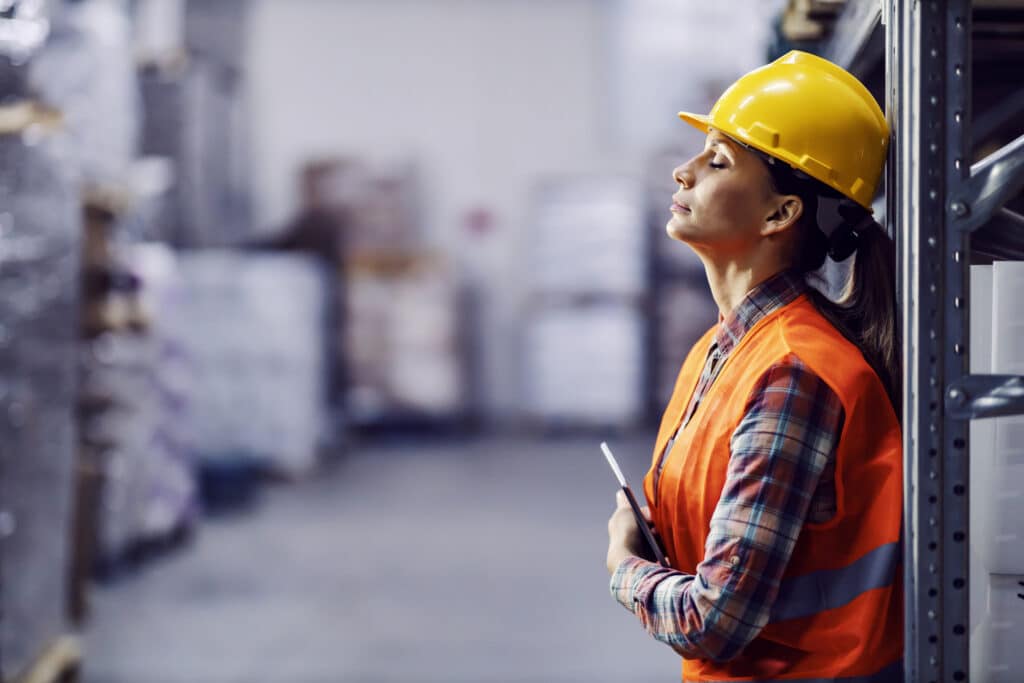 Female worker in a warehouse wearing a hard hat and high-visibility vest.